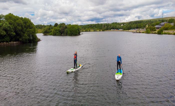 Visitors enjoying standup paddleboarding on the lake at Parc Bryn Bach.